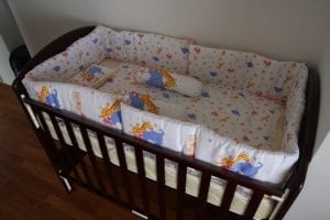 a wooden baby crib with mattress and side protectors to keep the baby safe inside. A crib takes a lot of space in the room.