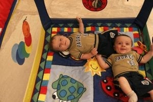 Two babies on a baby crib with a lot of space having their fun crib moment