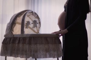 A pregnant woman holding a bassinet thinking how lucky she is for choosing it instead of a crib that may take a lot of space.