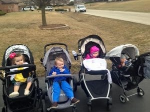 Four kids in individual carriages on a neighborhood sidewalk, with houses and leafless trees in the background. The scene captures the essence of suburban life, where open skies and friendly streets become playgrounds of discovery.