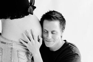 husband piercing his ears to wife's baby bump, listening for a newborn baby heartbeat from his wife's tummy