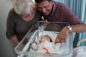 grandmother and grandfather touching a newborn baby from the crib - such a joyous and momentous event in their life