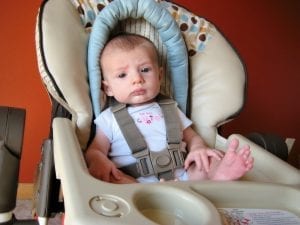 A baby seating on a high chair - the top high chair in the market