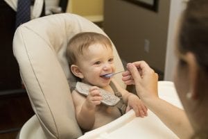 A smiling baby is on the best high chair while her mother is feeding her.