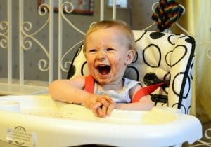 A laughing baby is sitting on a high chair with arm straps.