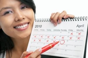 A photo of a smiling woman pointing to a date on a calendar