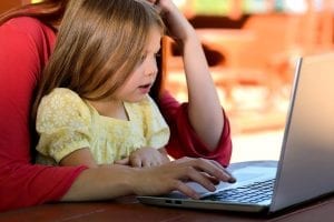 A little girl using her laptop with her parent