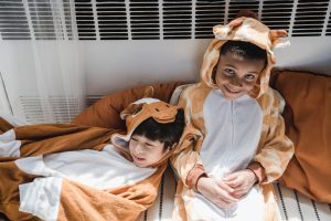 Two kids in onesie outfits of cute style smile and talk to each while playing inside the room. 