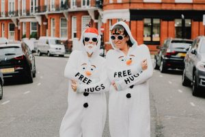 Two people in matching snowman costumes. They are standing on the street surrounded by parked cars.