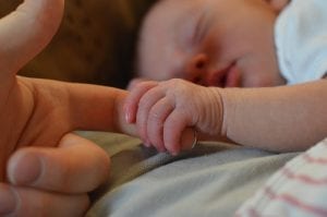 A child holding the finger of her mom. This baby is beautifully sleeping and is feeling very comfortable in her pram.