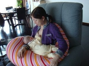 A mother setting on a glider chair providing comfort to herself while breast feeding to a baby. The glider is gray and big.