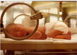 best newborn diapers - This newborn is sleeping comfortable, with his tummy against the surface of the incubator. Baby like this needs the best disposable diapers that are hypoallergenic. The face of the baby is clearly visible from the incubator's window. 