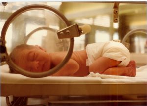 best newborn diapers - This newborn is sleeping comfortable, with his tummy against the surface of the incubator. Baby like this needs the best disposable diapers that are hypoallergenic. The face of the baby is clearly visible from the incubator's window.