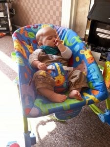 A baby sleeping soundly on a Fisher-Price Rock 'n Play Sleeper while he play with his thumb