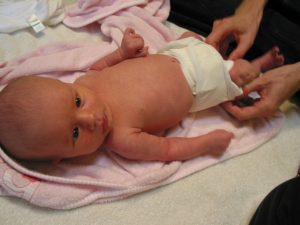 A newborn baby wearing a diaper. The baby is staring at something while diapering.