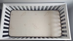 A white baby crib with foam mattress.