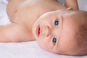 A baby lying on the bed, eyes staring at the camera