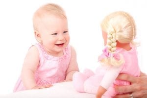 Best girls toy: A young female child, dressed in a charming shade of pink, is thoroughly engrossed in observing and interacting with her baby doll.