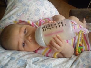 A photo of a baby holding and drinking a bottle of baby formula