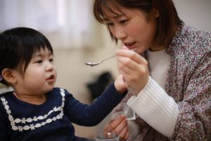 A mom making a toddler take a liquid multivitamin