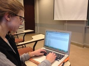 A young woman engrossed in her laptop, fingers dancing on the keyboard. She sits in a cozy spot, surrounded by warm lighting, with a focused expression. The laptop screen illuminates her face, revealing a mix of concentration and excitement. 