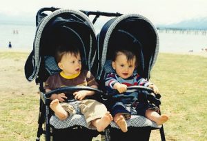 Two kids riding a double stroller while enjoying the early morning sunrise near the lake. 