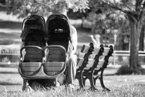 An empty pram is placed near the bench of a clean and grassy park. 