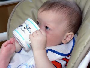 In the gentle grasp of small, curious hands, a child is drinking from a toddler cup. With wide, curious eyes gleaming with discovery, this child takes in nourishment in measured sips rewarding their thirst with a satisfying quench.