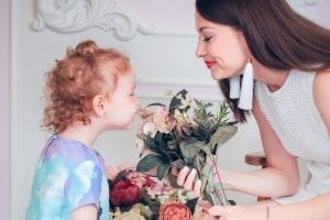 Mom letting her daughter smel the flowers What are the best bags for moms with toddlers?