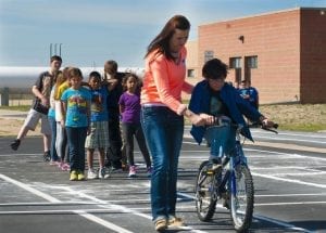 One of the kids having the best experience in riding a bike while being guided by a teacher.