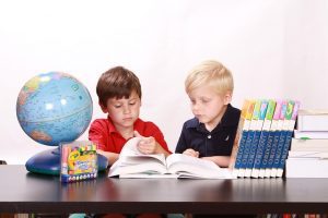 Two boys studying from a book for their class, with a globe and colorful markers on the table.
