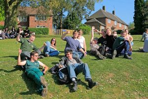 A group of individuals wearing their boots, who are having fun, laughing, and looking at each other with their arms up in the air, while laying outside of their school. 