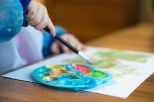 A boy painting with a brush, carefully selecting colors from a palette for his year-end art project.