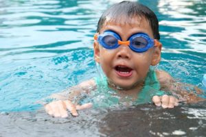 A kid in the pool wearing goggles.