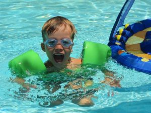 Happy kid in the pool wearing goggles and floaters