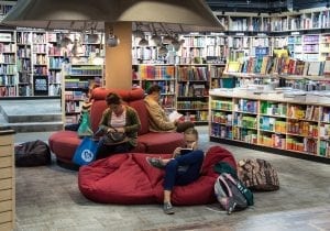 A public library with diverse individuals including a third grade child find comfort on a plush couch, each absorbed in the pages of captivating books.