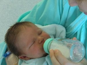 Mother feeding her newborn with formula through a feeding bottle.