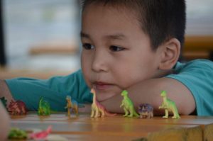 A seven year old kid wearing a green shirt plays with his dinosaur toys.