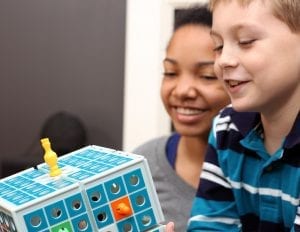 Two kids smile while playing with their toy in a brightly lit room.