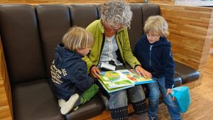 An elderly woman reading a book to two young boys on a couch, a moment of learning and bonding for the year.