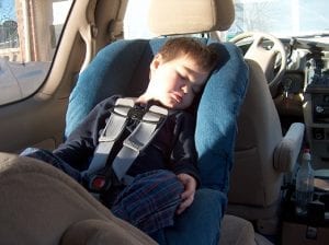 A handsome baby boy comfortably sleeping on the back seat of the car with a seat belt on a rear-facing car seat.