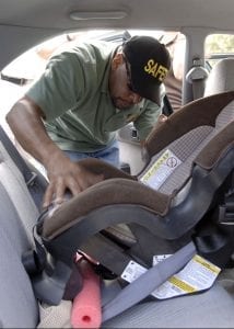 A man in a polo shirt and a black hat is installing a baby car seat on the back seat of the car. This is to ensure that the baby car seat and the back seat of the car is compatible. 