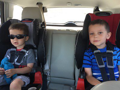Two boys sitting on the back seat of the car with their seat belt on their soft and comfy baby car seat. 
