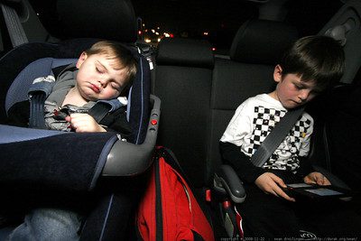 Baby car seat. A kid age 3 is on the back seat of the car with his brother while sleeping silently on the baby car seat with a seat belt.