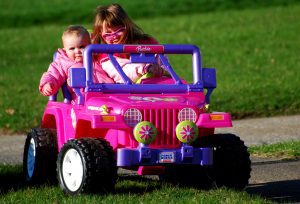 Power Wheels: Two children in a pink Power Wheels Jeep enjoy a sunny day outdoors.