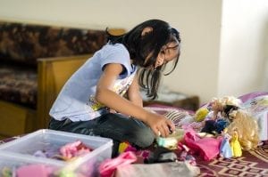 girl silently playing with her dolls and dresses on her bed