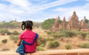 A 9-year-old young lady with a bright red shirt sits in awe, her eyes fixed on a majestic castle in the distance. Her expression reflects a sense of wonder and excitement as she takes in the grandeur of the castle. The girl's red shirt stands out against the backdrop, adding a vibrant pop of color to the scene. Her posture suggests that she is fully engrossed for that moment, captivated by the enchanting sight before her.