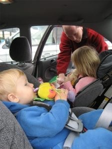 A father buckles the seat belts of his two children - 