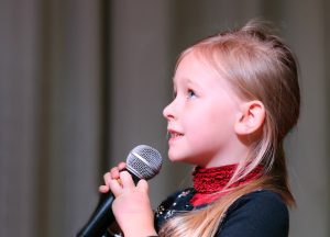 A little kid holding a microphone singing.