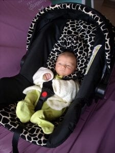 An infant rests comfortably in his black car seat